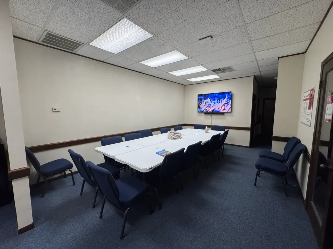 The Bible Study Room at the Seek the City prayer room — long white tables ringed with chairs beneath bright ceiling lights.